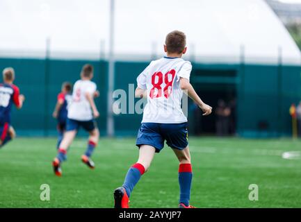 Les garçons de sport blanc et bleu jouent au football sur le terrain, dribbles ball. Jeunes joueurs de football avec balle sur l'herbe verte. Entraînement, football l Banque D'Images