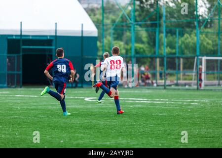 Les garçons de sport blanc et bleu jouent au football sur le terrain, dribbles ball. Jeunes joueurs de football avec balle sur l'herbe verte. Entraînement, football l Banque D'Images