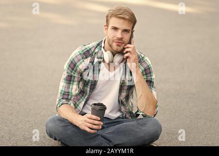 Appel important. appel téléphonique. écouter la musique. ebook concept. homme Chemise à carreaux. élève se détendre et recharger. café d'aller. guy boire un café en plein air. L'homme s'asseoir sur le sol. étudiant insouciant en casque. Banque D'Images