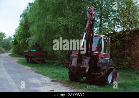 vieux tracteur rouillé rouge dans un champ proche de la route. Banque D'Images