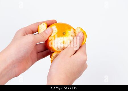 La main de la femme décolle une orange. Main pour nettoyer le mandarin. Isolé sur fond blanc. Alpha Banque D'Images