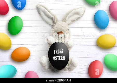 Lapin farci avec message 'Hapy Easter' en allemand et de nombreux oeufs de pâques sur fond en bois blanc Banque D'Images