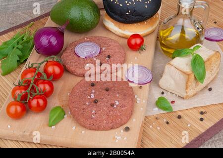 Deux hamburgers de légumes crus sur une planche en bois avec sel, poivre, huile d'olive et légumes pour la cuisson Banque D'Images