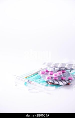 Pilules multicolores en plaquettes thermoformées, thermomètre, masque chirurgical protecteur, seringue sur fond blanc. Attaque virale. Espace de copie. Bouquet de médicaments, froid f Banque D'Images