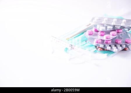 Pilules multicolores en plaquettes thermoformées, thermomètre, masque chirurgical protecteur, seringue sur fond blanc. Attaque virale. Espace de copie. Bouquet de médicaments, froid f Banque D'Images