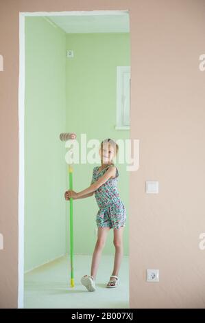 belle petite fille mince stand avec rouleau de peinture dans un nouvel appartement plat Banque D'Images