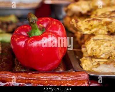 Des poivrons rouges rôtis colorés et une variété de saucisses grillées à la viande empilent sur des plateaux au festival de la nourriture de rue, foyer sélectif, gros plan. Barre huileuse malsaine Banque D'Images