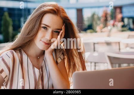 Une jolie fille avec des cheveux rouges et des cornichons regardant pacifiquement vous pose dehors et pense aux plans futurs Banque D'Images