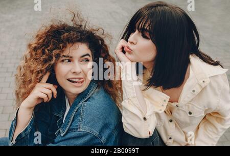 La vue supérieure de deux filles expressives avec des cheveux frisés qui se posent à l'extérieur ayant un beau temps ensemble Banque D'Images