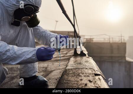 Chercheur travaillant sur le toit du bâtiment élevé, effectuant des essais de laboratoire à l'aide de réactif bleu dans une fiole en verre, des brucelles et de la pierre, instantané de gros plan. Concept de problème environnemental Banque D'Images