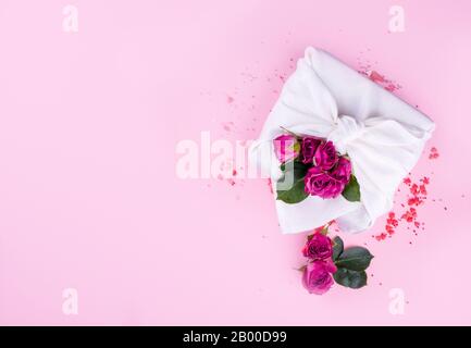 Le cadeau est emballé dans le style de furoshiki, avec des coeurs et des fleurs sur un fond rose. Un cadeau de Saint-Valentin. Banque D'Images