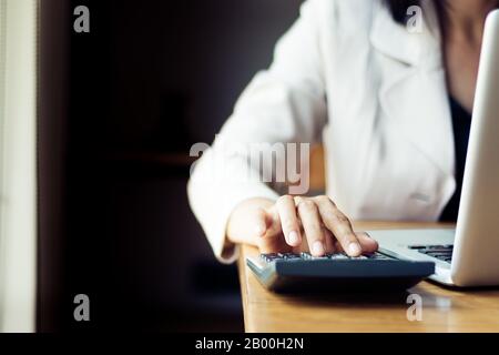 Femme d'affaires asiatique utilisant la calculatrice pour la comptabilité et l'analyse des investissements devant l'ordinateur portable au bureau. Banque , épargne , ac Banque D'Images