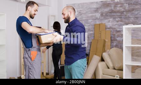 Le service de l'homme arrivant avec des cases et des documents à signer. Beau jeune couple le déménagement. Banque D'Images