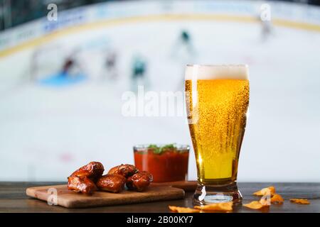 Ailes épicées de poulet barbecue, salsa de tomates, nachos et bière sur table de bar en bois sombre. Hockey sur fond, haute résolution Banque D'Images