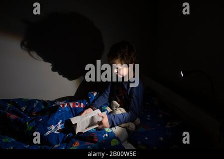 Garçon de 6 ans lisant un livre d'Enid Blyton à l'heure de la nuit dans sa chambre, Angleterre, Royaume-Uni Banque D'Images