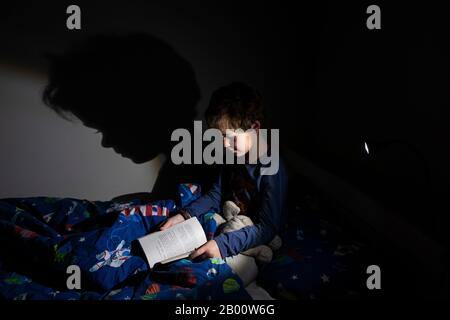 Garçon de 6 ans lisant un livre d'Enid Blyton à l'heure de la nuit dans sa chambre, Angleterre, Royaume-Uni Banque D'Images