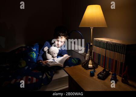 Garçon de 6 ans lisant un livre d'Enid Blyton à l'heure de la nuit dans sa chambre, Angleterre, Royaume-Uni Banque D'Images