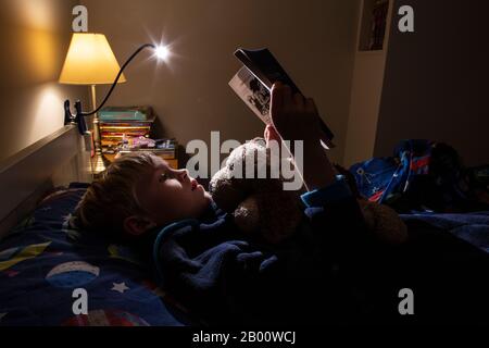 Garçon de 9 ans lisant un livre d'Enid Blyton à l'heure de la nuit dans sa chambre, Angleterre, Royaume-Uni Banque D'Images