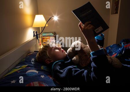 Garçon de 9 ans lisant un livre d'Enid Blyton à l'heure de la nuit dans sa chambre, Angleterre, Royaume-Uni Banque D'Images