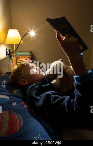 Garçon de 9 ans lisant un livre d'Enid Blyton à l'heure de la nuit dans sa chambre, Angleterre, Royaume-Uni Banque D'Images