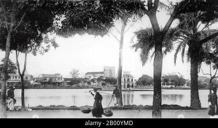 Vietnam : Lac Hoan Kiem, Hanoï (début du XXe siècle). Le lac Hoan Kiem, qui signifie « le lac de l'épée retournée » est situé dans le centre historique de Hanoi et est aujourd'hui l'un des sites les plus pittoresques et les plus connus de la capitale vietnamienne. Selon la légende, le lac porte le nom d'une épée magique appartenant à l'empereur le Loi, qui lui a apporté la victoire dans sa révolte contre la dynastie Ming chinoise. Un pont en bois peint en rouge appelé le pont Huc relie l'île de Jade à la rive en traversant le lac. Le temple Ngoc son (temple de montagne de Jade) se dresse sur l'île. Banque D'Images