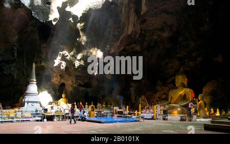 Thaïlande: Fidèles à l'intérieur de la caverne principale à Tham Khao Luang, Phetchaburi. Tham Khao Luang est une grande grotte composée de trois chambres reliées et se distingue par de nombreuses stalactites suspendues et des images de Bouddha, y compris un phra non ou Bouddha couché. La principale image de bronze a été moulée sur les ordres du roi Chulalongkorn (Rama V) et dédiée à ses illustres prédécesseurs, les Rois Rama III et Rama IV Il y a une ouverture naturelle dans le plafond de la deuxième chambre principale, par laquelle la lumière du jour éclaire les images à l'intérieur. Banque D'Images