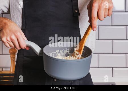 Man's hands close-up holding une casserole et remuer avec une cuillère de bois. Banque D'Images