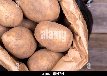 Gros plan de pommes de terre dans un sac de papier brun et noir sur fond en bois. Banque D'Images