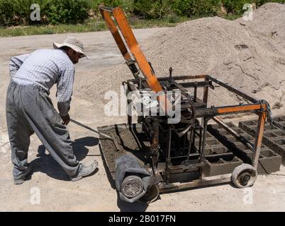 Shahin Dezh, Iran - 15 mai 2019: Un travailleur qui fait des briques avec une machine et du ciment, Iran. Banque D'Images