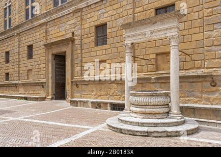 Vieux puits dans la place principale de Pienza. Le puits de travertin du Rossellino et le devant du Palazzo Piccolomini à Pienza, Toscane, Italie. Banque D'Images