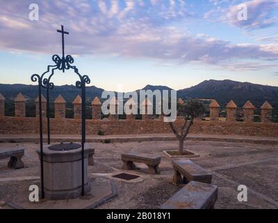 Cloître avec bancs et bien dans le Sanctuaire de Sant Salvador Arta, Majorque (Majorque) sur les montagnes d'arrière-plan et les nuages après le coucher du soleil Banque D'Images