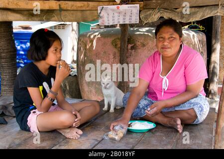 Thaïlande: Une mère et une fille Urak Lawoi (Sea Gypsy) mangent le déjeuner, Laem Tukkae, Phuket. Les «sea Gypsies» ou Moken de la mer d'Andaman, connus en thaï sous le nom de chao thalae ou de «peuple de la mer», sont divisés en trois groupes. Ils sont entre 4 000 et 5 000, ils ne vivent que sur la côte, soit dans des huttes au bord de la côte, soit dans des bateaux qui sillonnent les eaux côtières de l'archipel de Mergui en Birmanie aux îles Tarutao en Thaïlande du Sud. Le plus grand groupe de Gypsy de mer est le Urak Lawoi, qui se chiffre autour de 3 000. Ils vivent dans des cabanes simples sur des plages s'étendant au sud de Phuket aux îles Tarutao. Banque D'Images