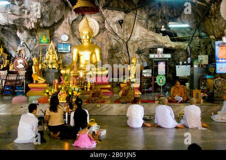 Thaïlande : moines bouddhistes, nonnes et autres dévots, Wat Tham Seua, ville de Krabi, province de Krabi, sud de la Thaïlande. Wat Tham Seua, le « Temple de la grotte du tigre » est construit dans une grotte située dans une falaise calcaire. Entouré de résidences individuelles de moines, c'est l'un des temples forestiers les plus connus du sud de la Thaïlande. Le viharn principal ou salle de rassemblement se prolonge dans une longue grotte calcaire peu profonde affichant divers sombres rappels de mortalité comme contrepoids aux désirs mondains. À l'arrière de la grotte, un escalier en marbre mène à la « grotte du tigre » elle-même. Banque D'Images