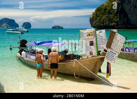 Thaïlande : les visiteurs achètent des collations à l'un des bateaux de restauration alignés sur la plage de Hat Tham Phra Nang, Krabi Coast Hat Tham Phra Nang, la «plage de la dame vénérée», est une belle plage de sable blanc à l'extrémité sud de la petite péninsule séparant Rai le East Beach de Rai Leh West Beach. La plage est considérée par beaucoup comme la plus belle de la région de Krabi, et aussi l'une des plus belles du sud de la Thaïlande. Composé de sable blanc et croquant et abrité par de hautes falaises de calcaire, le cadre idéal est rehaussé par des affleurements karstiques pointus et aux formes étranges. Banque D'Images