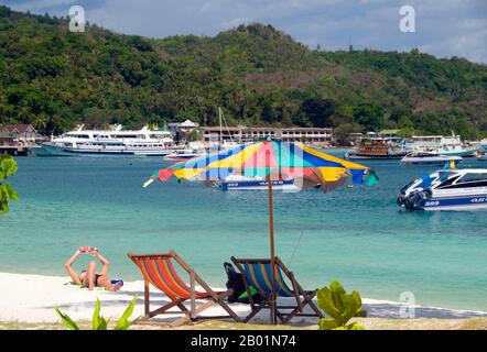 Thaïlande : détente à côté d'un parasol, Tonsai Bay, Tonsai Village (Ban ton Sai), Ko Phi Phi Don, Ko Phi Phi. Ko Phi Phi se compose de deux îles, Phi Phi Leh et Phi Phi Don, situées au sud-est de Phuket. Tous deux font partie du parc marin national Hat Noppharat Thara Ko Phi Phi. Situé dans le centre de la mer de Phuket, Ko Phi Phi est presque à égale distance de Phuket et de Krabi et peut être atteint en bateau en environ deux heures. Phi Phi Don est la plus grande des deux îles, avec des collines pittoresques, des falaises abruptes, des plages de soie, des eaux azur et une vie remarquable d'oiseaux et de mer. Banque D'Images