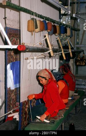 Chine : tisserands de tapis ouïghours, usine de tapis, Khotan, Xinjiang. Khotan retrace son histoire au moins jusqu'au IIIe siècle av. J.-C., lorsque le fils aîné de l'empereur indien Asoka s'est installé ici. Il était d'une grande importance sur la route de la soie, et on prétend avoir été le premier endroit en dehors de la Chine à avoir cultivé la soie. Il se trouve à cheval sur les rivières Karakash ou «Jade noir» et Yurungkash ou «Jade blanc», qui se rejoignent ici pour former le Khotan Darya, et est célèbre pour son jade depuis plus de deux millénaires. Banque D'Images