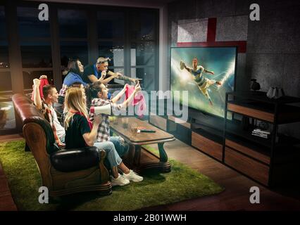 Groupe d'amis regardant la télévision, match, championnat, jeux de sport. Des hommes et des femmes émotionnels applaudisdisent avec drapeau l'équipe de rugby préférée de l'Angleterre. Concept d'amitié, de sport, de compétition, d'émotions. Banque D'Images