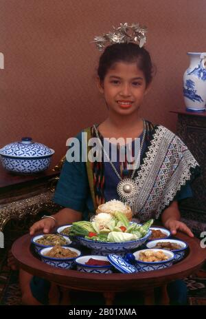 Thaïlande : une fille en vêtements traditionnels Lanna propose un dîner khantoke, Chiang mai, dans le nord de la Thaïlande. Le nord de la Thaïlande a hérité de l'héritage culinaire du Royaume autrefois puissant de LAN Na, avec des liens avec la Birmanie voisine et la province chinoise du Yunnan. Une caractéristique remarquable est l'utilisation répandue de tomates dans les currys et autres plats cuisinés - ailleurs en Thaïlande, la tomate est généralement considérée comme un légume à salade. Les plats distinctifs comprennent le soja khao - un plat de nouilles succulent introduit par les caravaniers musulmans de Chine. Banque D'Images