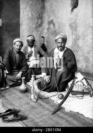 Palestine : des hommes palestiniens se relaxant dans un café de Jérusalem tout en fumant des conduites d'eau, v. 1920. Palestine est un nom donné à la région géographique entre la mer Méditerranée et le Jourdain. La région est également connue comme la Terre d'Israël, la Terre Sainte et le Levant Sud. En 1832, la Palestine a été conquise par l'Égypte de Muhammad Ali, mais en 1840, la Grande-Bretagne est intervenue et a rendu le contrôle du Levant aux Ottomans en échange de nouvelles capitulations. La fin du XIXe siècle voit le début de l'immigration sioniste et la renaissance de la langue hébraïque. Banque D'Images