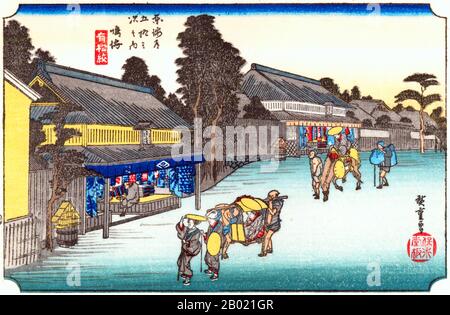 Japon : 'Station Forty : Narumi, Un endroit célèbre pour son tissu'. Estampe sur bois ukiyo-e de la série 'cinquante-trois stations de la route de Tôkaidô' par Utagawa Hiroshige (1797-1858), vers 1834. Narumi : une femme portée dans un kago et deux autres marchant devant, suivi par un homme à cheval et deux préposés, passant devant deux grandes boutiques ouvertes dans la rue principale, où des tissus teints sont vendus. Sur la façade de la boutique la plus proche se trouve le monogramme Hiro au centre, et celui de l'éditeur, Take-no-Uchi, de chaque côté. Banque D'Images