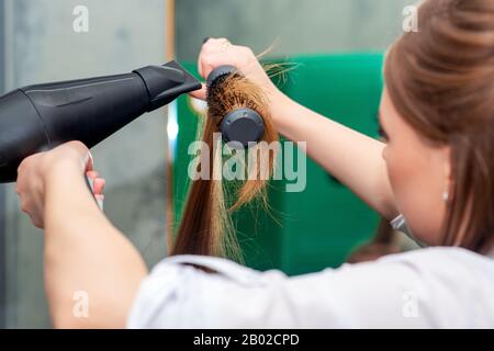 Coiffeur séchage cheveux longs brun avec sèche-cheveux et brosse ronde, gros plan. Banque D'Images