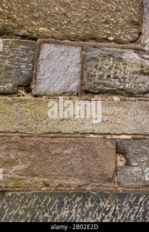 Les roches et les pierres grises et brunes de cet ancien mur sont coudées et penchées d'un côté. Il est plein de texture et d'intérêt visuel. Banque D'Images