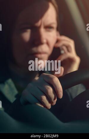 Femme d'affaires parlant sur le téléphone mobile dans la voiture tout en conduisant au travail, foyer sélectif Banque D'Images