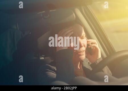 Femme d'affaires parlant sur le téléphone mobile dans la voiture tout en conduisant au travail, foyer sélectif Banque D'Images