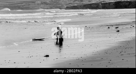 Un surfeur déjecté ou fatigué est assis sur une boîte avec son surf, Portreath, Cornwall, Angleterre Banque D'Images