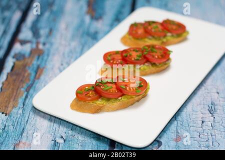 Sandwichs à surface ouverte avec tartiner d'avocat, amandes de tournesol, tranches de tomate et ciboulette en dés, disposés sur un plateau de service blanc. Mise au point sélective. Banque D'Images