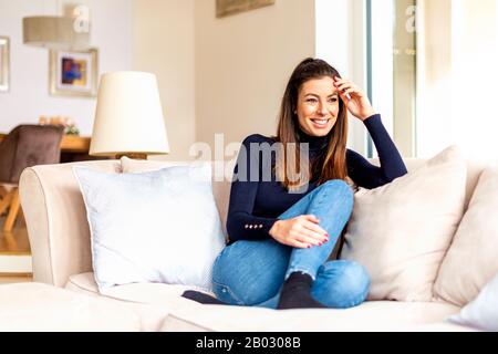 Photo pleine longueur d'une jolie femme rêvant tout en se reposant sur un canapé à la maison. Banque D'Images