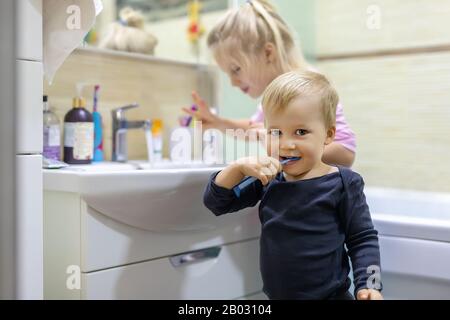 Deux adorables frères et sœurs blonds caucasiens se lavant le visage et la dent de nettoyage avec brosse à dents à la salle de bains à la maison le matin. Petit frère enfants et Banque D'Images