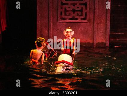 Water Puppetry ou Múa rối nước, littéralement "marionnettes qui dansent sur l'eau" est originaire du Delta de la rivière Rouge. Les marionnettes sont sculptées de bois résistant à l'eau pour représenter les styles de vie ruraux traditionnels et les créatures mythiques. Debout derrière la scène aquatique, au fond de la taille dans l'eau, les marionnettes cachées manœuvrent habilement leurs charges en bois à la musique d'un orchestre traditionnel. Banque D'Images