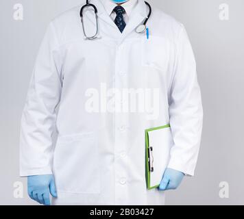 médecin masculin dans un manteau blanc, gants en latex bleu, stéthoscope suspendu sur son cou, médecin tenant un support en papier vert avec une feuille blanche vierge Banque D'Images